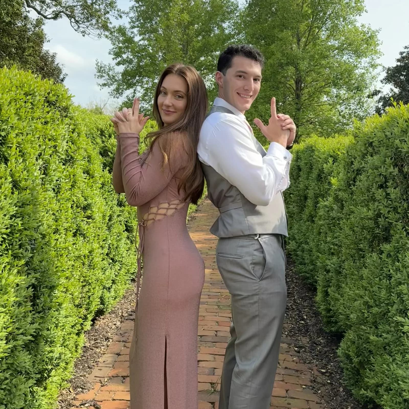 Meaghan and Roman posing back to back along a hedge